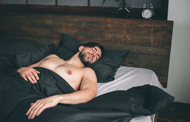 Portrait of fit male model asleep in luxurious bedroom bathed in bright warm morning window light