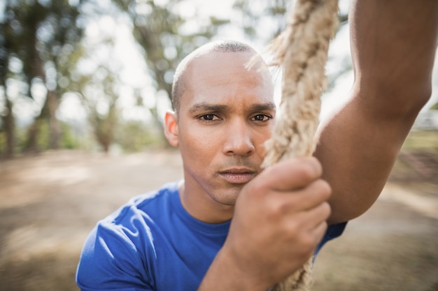 Portrait of fit man climbing rope during obstacle course in boot camp