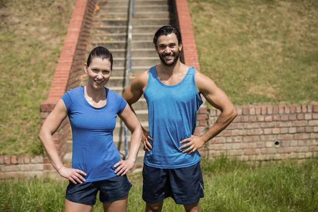 Portrait of fit man and woman standing with hands on hip against staircase in boot camp