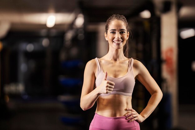 Portrait of a fit sportswoman giving thumbs up in a gym