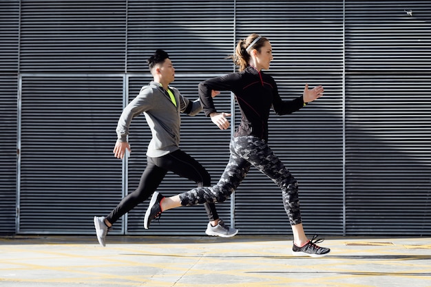 Portrait of fit and sporty couple running in the street.