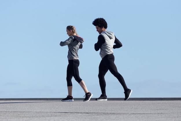 Portrait of fit and sporty couple running in the street.