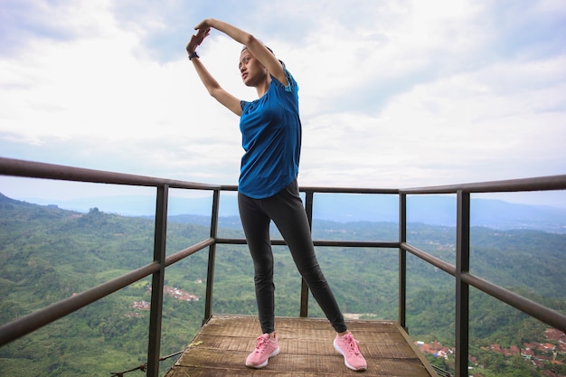 Портрет подходящей и спортивной молодой азиатской женщины, делающей протягивание на горе.