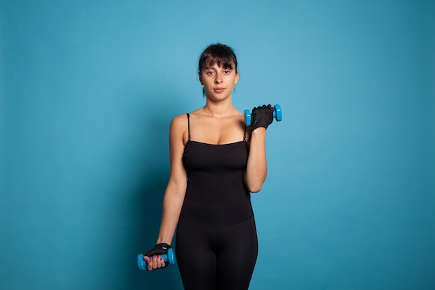 Portrait of fit trainer looking into camera while doing stretching exercises using sport dumbbells in studio. Active person working at healthy lifestyle training body endurance