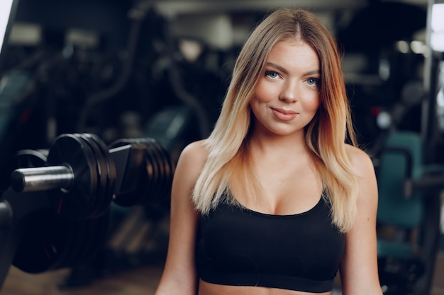 Portrait of a fit young blonde woman in black sport bra in gym