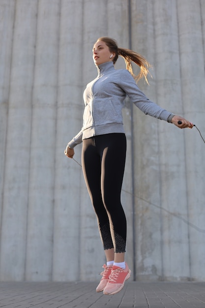 Ritratto di giovane donna in forma con corda per saltare all'aperto. fitness femminile facendo saltare l'allenamento all'aperto all'alba o al tramonto.