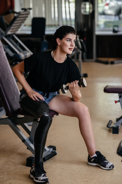 Portrait of fitness disabled woman in tracksuit doing crossfit exercises and lifting dumbbell in gym