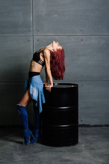 Portrait of fitness woman on cement concrete background, near a black barrel.