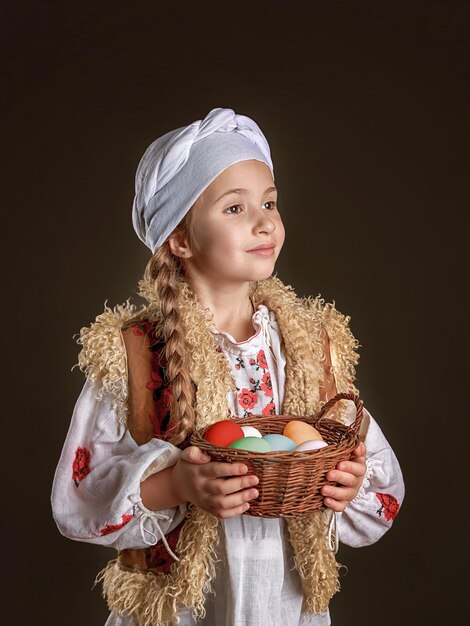 Portrait of a fiveyearold girl with a scythe in a national vintage ukrainian costume she is holding a basket of colored easter eggs closeup portrait