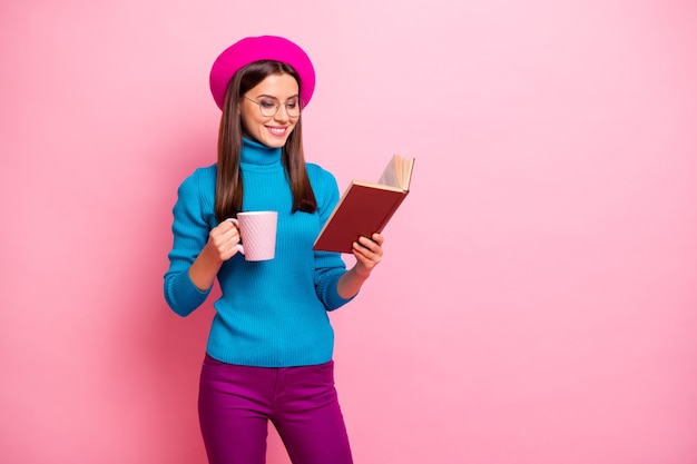 Портрет сосредоточенной веселой девушки на выходных, чтение учебника, кружка с горячим напитком, фиолетовые брюки.