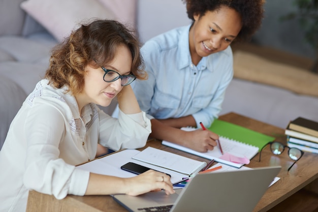 Portrait of focused female teacher in glasses helping teen schoolgirl with homework sitting at the