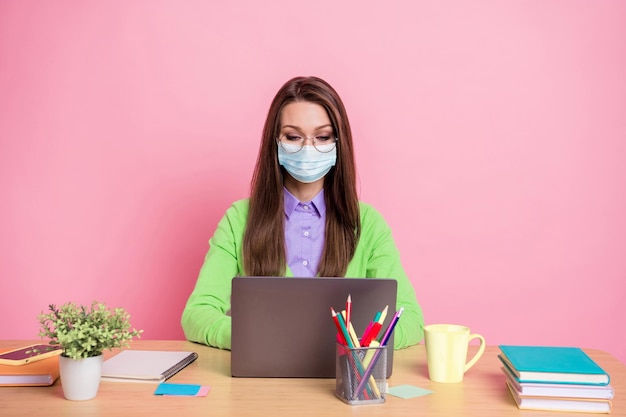 Portrait of focused girl sit table work remote laptop wear green shirt medical mask isolated pastel color background