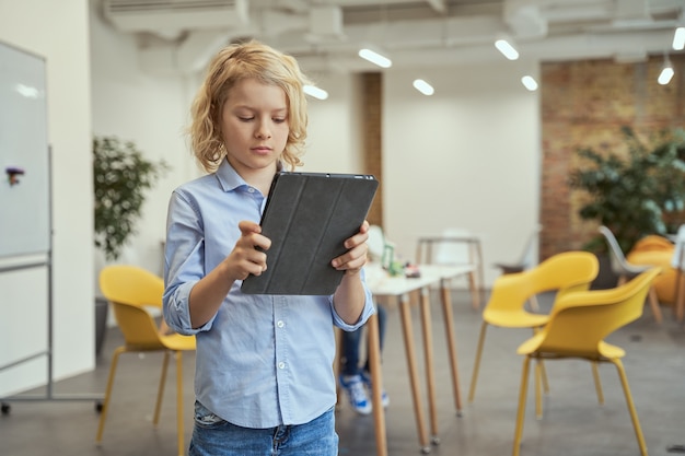 Portrait of focused little boy using tablet pc while posing for camera during stem classes