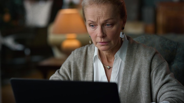 Портрет сосредоточенной старой женщины, работающей на ноутбуке в винтажной гостиной Клоуз-ап задумчивая старшая леди, ищущая ноутбук в роскошном доме Серьезная бизнес-женщина, думающая в помещении