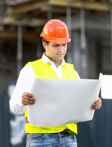 Photo portrait of foreman reading blueprints against scaffolding at building site