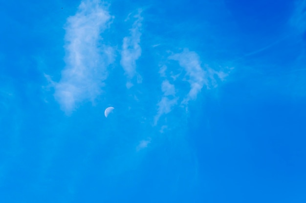 Portrait format image of a distant half moon isolated on a blue sky