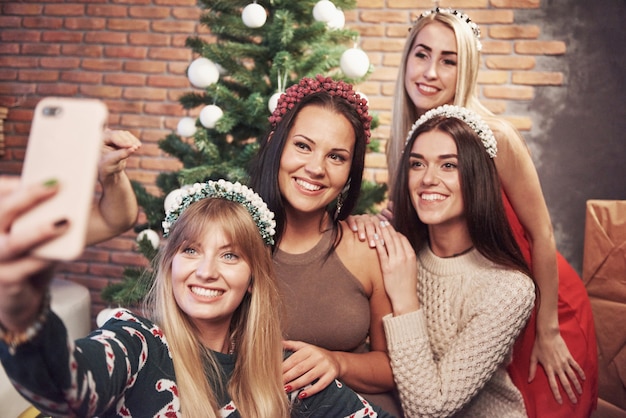 Portrait of four smiling girl with corolla on the head make selfie photo. New year's feeling. Merry christmas