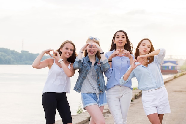 Portrait Of Four Young Women In Studio Standing In Line and show heart gesture together with arms outdoor