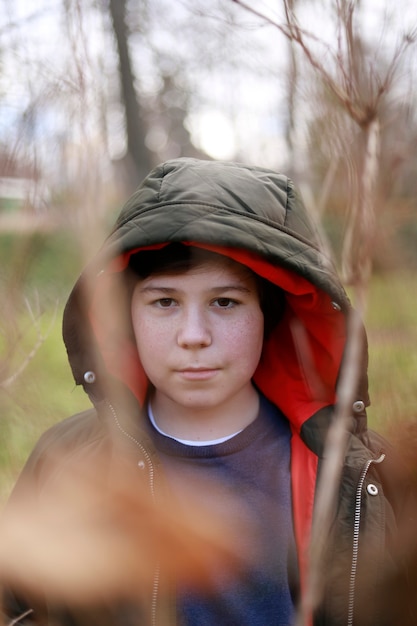 Photo portrait of freckled boy looking at camera with coat in park