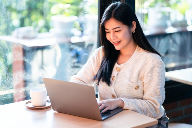 Ritratto di affari freelance bello sorriso positivo giovane donna asiatica online che lavora con il computer portatile a casa nel soggiorno all'interno o il cafebusiness lifestyle