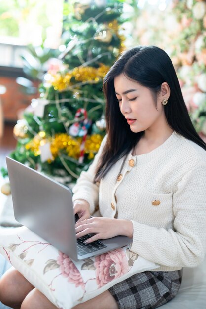 Portrait freelance business beautiful positive smile young asian woman online working with laptop computer at home in the living room indoors Decoration During Christmas xmas and New Year holidays