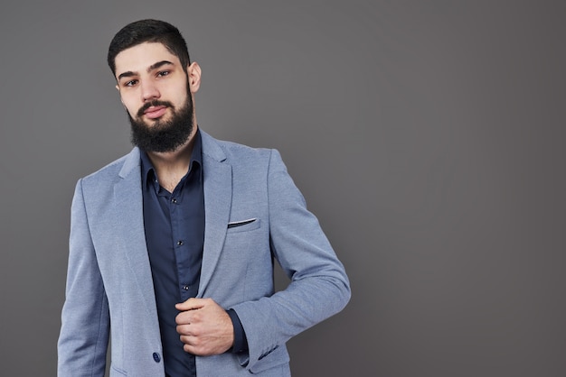 Portrait of freelancer man with beard in jacket standing against gray