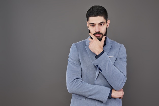 Portrait of freelancer man with beard in jacket standing on gray backdrop