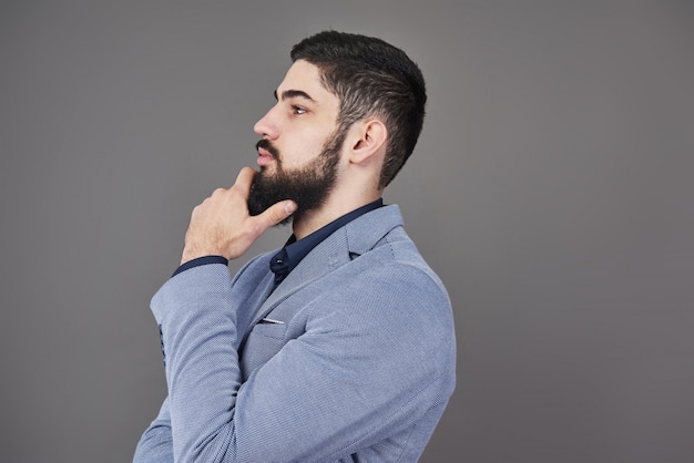 Portrait of freelancer man with beard in jacket standing on gray backdrop