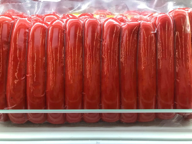 Photo portrait of fresh and thick red sausages packaged in plastic neatly lined up on a supermarket shelf