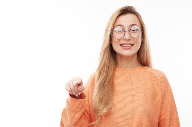 Portrait of friendly blonde girl chooses you points finger at the camera isolated on white background