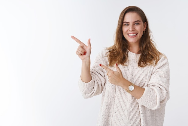 Ritratto amichevole splendida donna affascinante che indossa un maglione alla moda sciolto che punta il dito indice sinistro sorridente