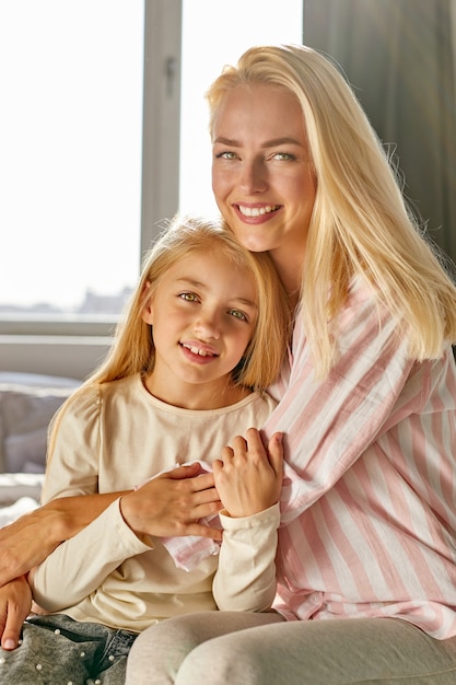 portrait of friendly mother and child girl in bedroom looking at camera posing, hugging. good