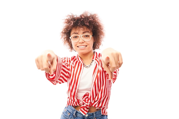 Photo portrait of friendly positive curly girl chooses you points finger at the camera isolated on white background