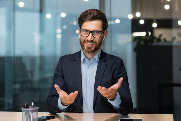 Portrait of a friendly young handsome man sitting in the office at the table wearing headphones and