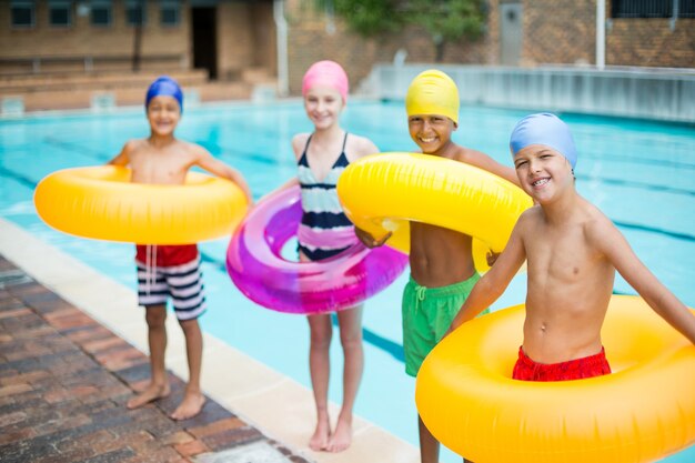 Portrait of friends carrying inflatable rings at poolside