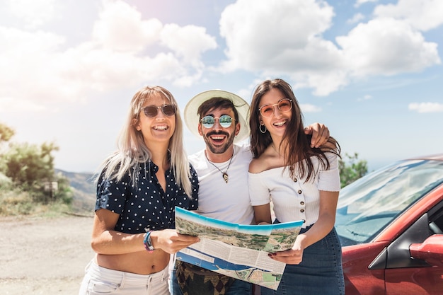 Photo portrait of friends standing near the car holding map