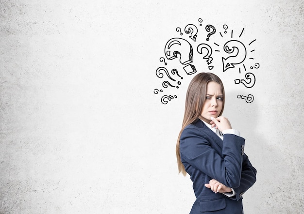 Portrait of a frowning woman in a business suit. She is plotting a suspicious action near a concrete wall with question marks on it. Mock up