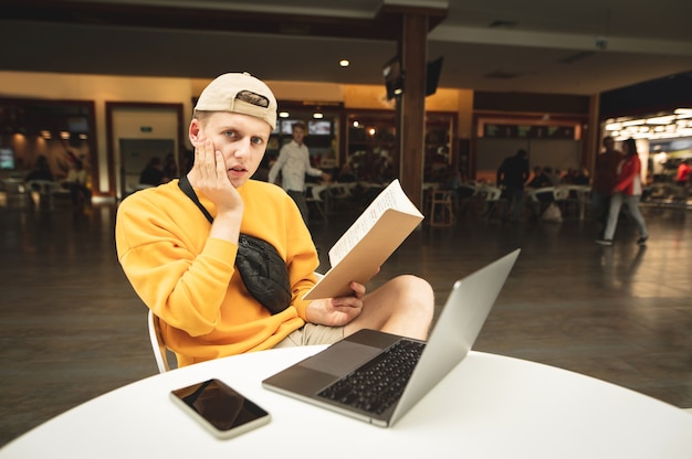 Portrait of a frustrated student sitting in a cafe with a laptop and notebook in his hand