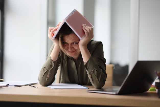 Portrait of frustrated woman covering head with book feeling tired and powerless female sitting