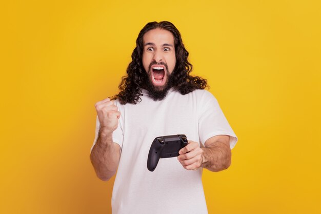 Portrait of funky addicted brunet guy hold gamepad play videogame celebrate victory on yellow background