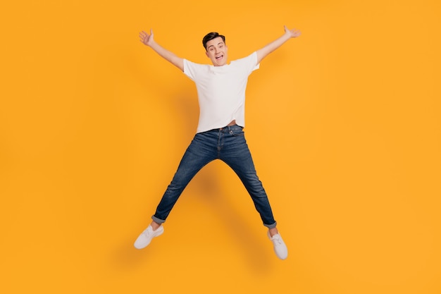 portrait of funky astonished guy jump make star shape have fun on yellow background
