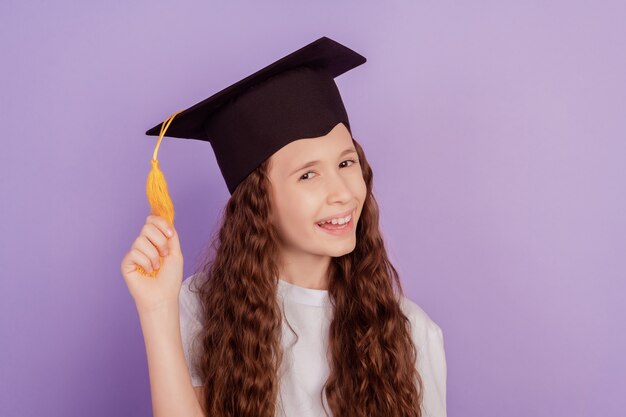 Portrait of funny adorable schoolgirl wear bachelor student hat play pompom on violet background