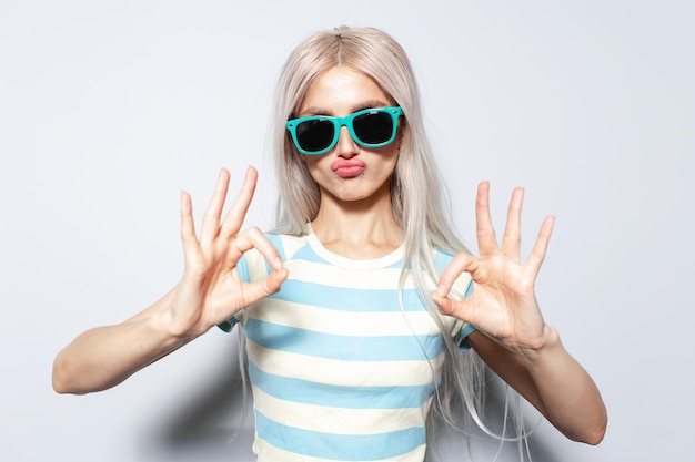 Portrait of funny blonde girl showing ok gesture with hands on white background