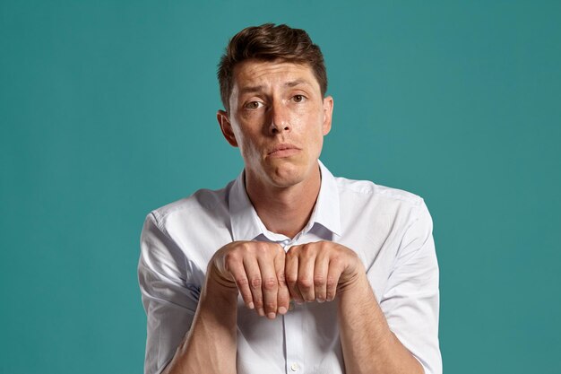 Portrait of a funny brunet male with brown eyes, wearing in a classic white shirt. He is fooling around while posing in a studio against a blue background. Concept of gesticulation and sincere emotion