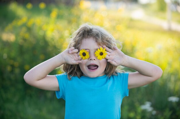 Portrait of a funny child boy holding flowers in front of eyes Close up caucasian kids face Closeup head of funny kid