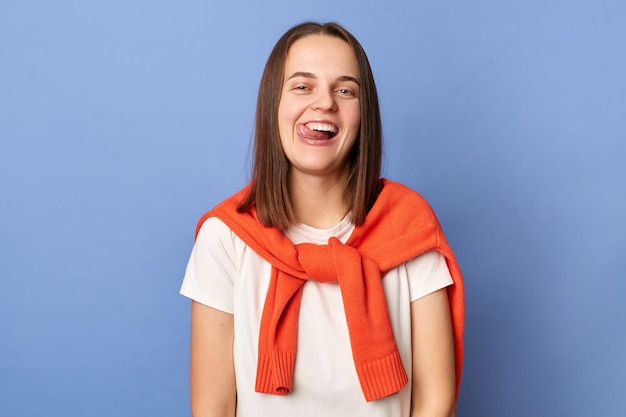 Portrait of funny childish attractive woman wearing casual style clothing standing isolated over blue background showing tongue out having fun fooling around
