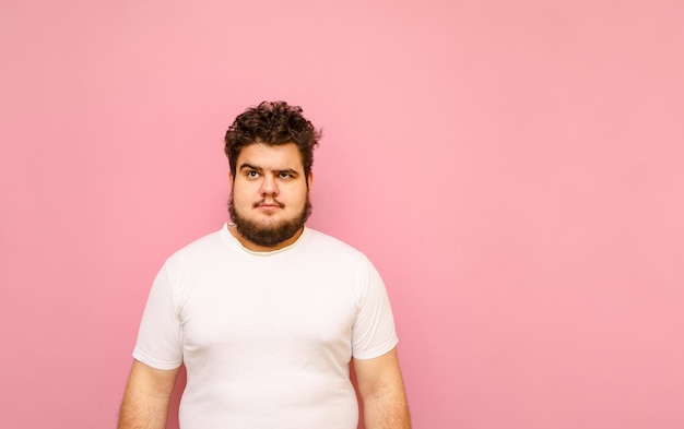 Portrait of funny curly fat man on pink background looks up at copy space with serious face