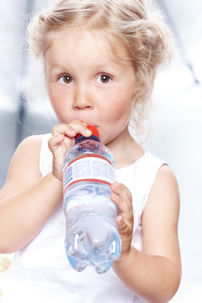 Portrait of a funny cute little girl in a casual dress, drink water while sitting in a studio.