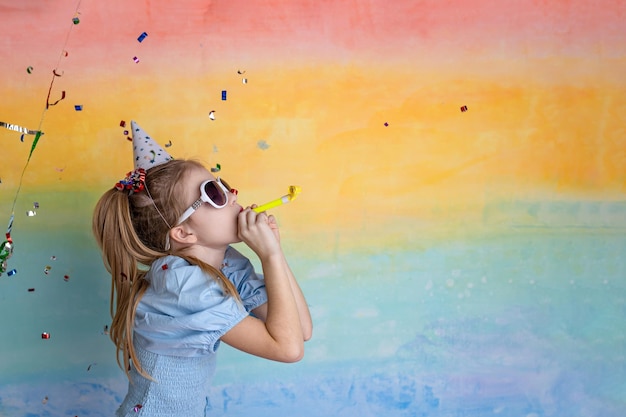 Portrait of funny girl in birthday hat and bright confetti on yellow background