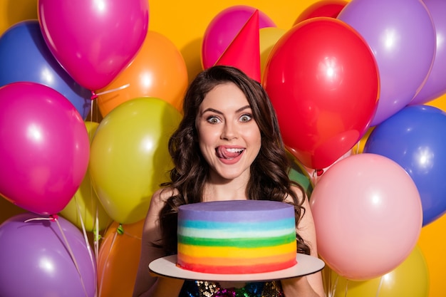 Portrait of funny girl have birthday anniversary hold big cake cant wait eat lick lips tongue have balloons wear sequins dress headwear cone isolated bright shine color background